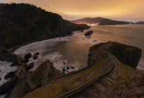 Olas golpeando contra puente de piedra medieval que conducen a una pequeña isla rocosa con la ermita de San Juan de Gaztelugatxe en la parte superior de la costa española en un día soleado con cielo azul en el fondo - foto de stock