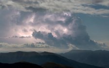 Gewitterwolken mit Blitz am blauen Himmel über dunklen Felsen — Stockfoto