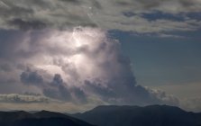Грім хмари з блискавкою на блакитному небі над темним скелястим гірським хребтом — стокове фото