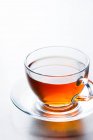 Primer plano de la taza de vidrio de té caliente aromático colocado en platillo en la mesa en la cafetería - foto de stock