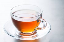 Closeup glass cup of aromatic hot tea placed on saucer on table in cafeteria — Stock Photo