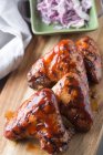 Ailes de poulet grillées délicieuses placées sur une planche de bois près de l'assiette avec oignon haché et serviette au restaurant — Photo de stock