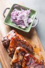Deliziose ali di pollo alla griglia poste su tavola di legno vicino al piatto con cipolla tritata e tovagliolo nel ristorante — Foto stock