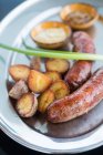 From above pieces of delicious grilled potatoes and juicy sausages with fresh scallion placed on metal plate near bowls with sauces in cafeteria — Stock Photo