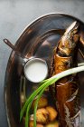 Vista dall'alto di gustoso pesce arrosto e patate servite con scalogno maturo e salsa alla panna su piatto di metallo nel ristorante — Foto stock