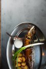Верхний вид вкусной жареной рыбы и картошки подается с спелым скалионом и сливочным соусом на металлической пластине в ресторане — стоковое фото