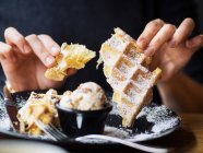 Persona anónima rompiendo pedazo de gofre suave sobre el plato con sabroso helado mientras está sentado en la mesa en el restaurante - foto de stock