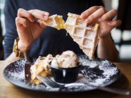 Анонімний чоловік розбиває шматочок м'якої вафельки на тарілці зі смачним морозивом, сидячи за столом у ресторані — стокове фото