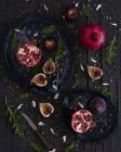 Ansicht von frisch geschnittenen Feigen und Granatäpfeln auf Tellern in der Nähe von Rucola und Messer auf dem Holztisch — Stockfoto