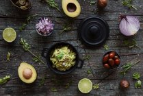 Vista superior de vários ingredientes frescos colocados na mesa de madeira perto do pote com guacamole gostoso — Fotografia de Stock