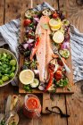 From above of delicious grilled salmon fillet garnished with assorted grilled vegetables served on wooden board on table with tomato sauce and bowl with salad — Stock Photo