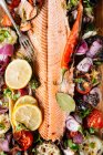 Сверху вкусное филе лосося на гриле, украшенное разнообразными овощами, подаваемыми на деревянной доске на столе с томатным соусом и миской с салатом — стоковое фото