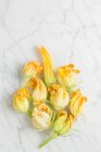 Top view of fresh yellow zucchini blossoms flowers arranged on white marble table in kitchen — Stock Photo
