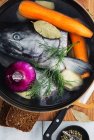 Vue du dessus du poisson cru et de l'oignon placés dans l'eau à l'intérieur d'une casserole avec des carottes et des pommes de terre complétées d'aneth et de laurier pendant la préparation de la soupe — Photo de stock