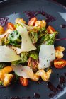 Сверху крупный план вкусного салата со свежими овощами и листьями с креветками и сыром подается на черной тарелке с соусом — стоковое фото