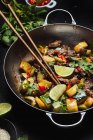 Dall'alto del wok piccante asiatico mescolare il piatto fritto con carne e zucchine guarnite con lime fresco e coriandolo. — Foto stock