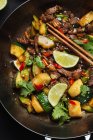 From above of Asian spicy wok stir fried dish with meat and zucchini garnished with fresh lime and cilantro — Stock Photo