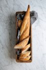 Vue de dessus de la délicieuse baguette fraîche tranchée servie sur un plateau en bois posé sur une table en marbre — Photo de stock