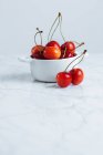 Ciliegia rossa matura fresca con steli in vaso di ceramica bianca appoggiati su tavolo di marmo contro parete bianca — Foto stock