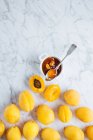 Draufsicht auf weißen Teller mit frischen gelben reifen Aprikosen auf weißem Marmortisch mit halbierter Aprikose und Marmelade im Glas — Stockfoto