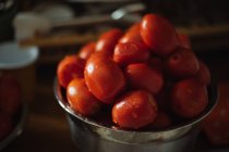 Dall'alto di pomodori di chicco d'uva rossi maturi freschi con gocce d'acqua in ciotola di metallo messe su tavolo di legno in cucina — Foto stock