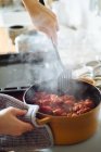 Врожай невизначена домогосподарка з шпателем, що тримає гарячу сковороду з вареними помідорами, готуючи смачний соус на кухні — стокове фото