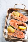 Vista superior de filetes de salmón fresco con condimentos aromáticos y rodajas de limón colocadas en una bandeja para hornear de metal - foto de stock