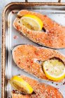 Верхний вид свежих стейков лосося с ароматической приправой и ломтиками лимона, размещенных на металлическом листе выпечки — стоковое фото