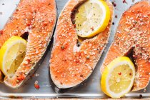 Vista superior de bifes de salmão frescos com tempero aromático e fatias de limão colocadas em assadeira metálica — Fotografia de Stock