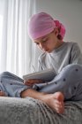 D'en bas enfant grave avec diagnostic de cancer prendre des notes tout en étant assis sur le lit dans la chambre — Photo de stock