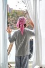 Vue arrière d'un enfant anonyme atteint d'un cancer portant un bandana rose et mettant la main sur la fenêtre dans la chambre — Photo de stock