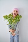 Menino alegre com diagnóstico de câncer vestindo bandana rosa e olhando para a câmera enquanto segurando vaso com flores e de pé na parede — Fotografia de Stock