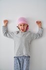 Хоробра маленька дитина з діагнозом раку дивиться на камеру і кричить, піднімаючи кулаки на сірому фоні — стокове фото