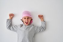 Храбрый маленький ребенок с диагнозом рак, смотрящий в камеру и кричащий, поднимая кулаки на сером фоне — стоковое фото