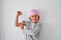 Храбрый маленький ребенок с диагнозом рак, смотрящий в камеру и кричащий, поднимая кулаки на сером фоне — стоковое фото