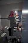 Vista trasera de un niño enfermo poniéndose pañuelo rosa delante del espejo en el baño - foto de stock