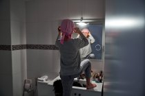 Visão traseira da criança doente colocando bandana rosa na frente do espelho no banheiro — Fotografia de Stock