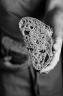 Урожай чоловічого пекаря в фартуху, що тримає нарізаний навпіл хліб свіжого здорового ремісника хліба — стокове фото