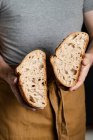Crop male baker in apron holding cut in half loaf of fresh healthy artisan bread — Stock Photo