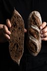 Cultivo panadero masculino en delantal sosteniendo cortado en media hogaza de pan fresco y saludable artesanal - foto de stock