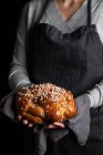 Cortar dona de casa em avental segurando apetitoso saboroso pão de trança caseiro com polvilhas — Fotografia de Stock