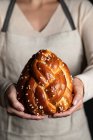 Crop housewife in apron holding appetizing tasty homemade braid bread with sprinkles — Stock Photo