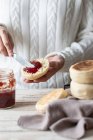 Primo piano di persona coltura diffusione gustosa marmellata di bacche rosse sul panino fresco tagliato fatto in casa — Foto stock
