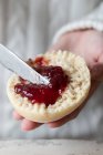 Closeup of crop person spreading yummy red berry jam on cut fresh homemade bun — Stock Photo