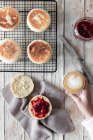From above of crop female having breakfast at wooden table with cup of cappuccino and fresh homemade buns with berry jam — Stock Photo