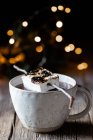 Marshmallow assado colocado em pau sobre xícara elegante de chocolate quente em mesa de madeira com brilhos no fundo escuro — Fotografia de Stock