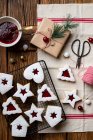 Верхний вид вкусного домашнего печенья различных форм с красным ягодным вареньем и белым сахарным порошком помещен на деревянный стол с посудой и декоративными элементами для празднования Рождества — стоковое фото