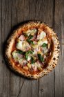 Blick von oben auf hausgemachte Pizza mit Schinken, Ananas, Basilikumblättern und Tomaten mit Käse auf Holzgrund — Stockfoto