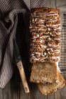 Вид зверху нарізаний апетитний домашній банановий хліб з горіхами та цукровою глазур'ю, розміщений на дерев'яному столі з ножем та скатертиною — стокове фото