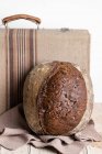 Healthy fresh homemade rye bread loaf placed on wooden table with cloth against black background — Stock Photo